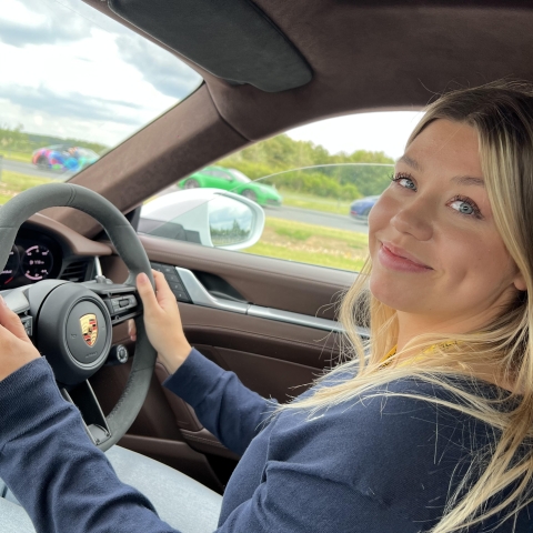 Daisy seated behind the wheel of a Porsche on test track