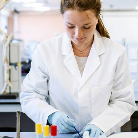 student with lab coat and long brown hair working on a petri dish