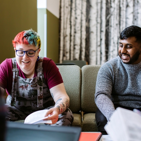 Two students sitting side by side on a sofa, smiling