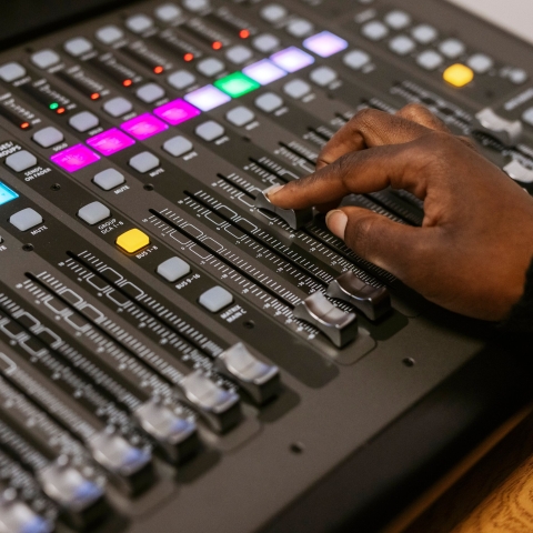 Close up of an audio mixer with a person's hand on a slider