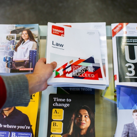 Career guidance books and leaflets on a desk with a person's hand picking one up