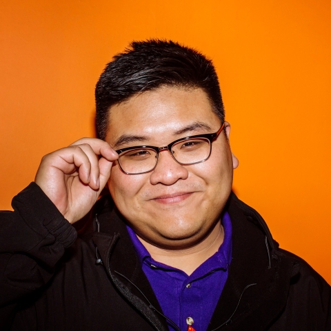 Smiling male student hold glasses in front of orange wall