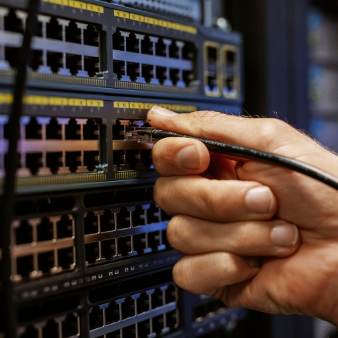 Student adjusts ethernet connections at a server board in Technology Facilities