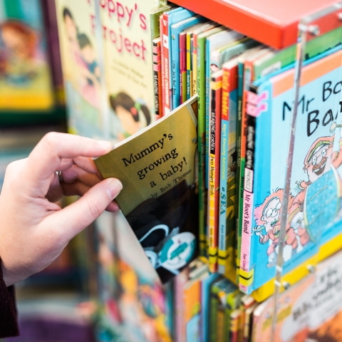 Teacher's hand extracting early years book from shelf
