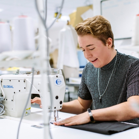 Textiles placement year student working in a fashion company. She is sat at a sewing machine working.
