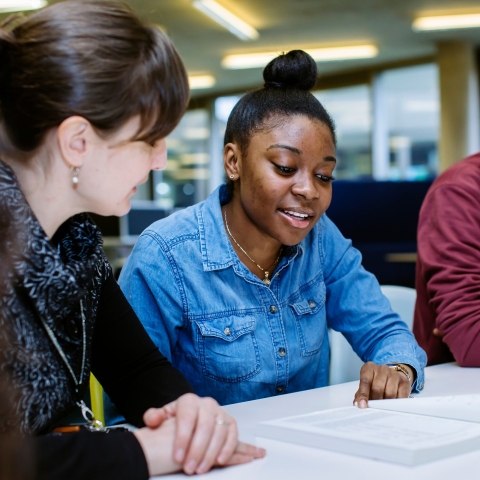 Staff member talking to two students at a table, supporting them with some of their work