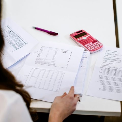 Female student looks over test pages with pink calculator on desk