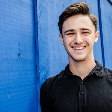 Josh Robinson smiling to camera wearing black t-shirt against blue wall