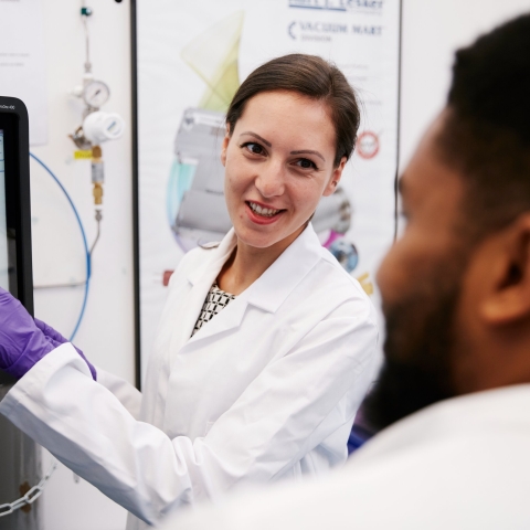Two students in lab coats consulting at a screen