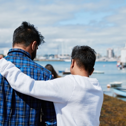 Two people looking out to sea, one with arm around the other
