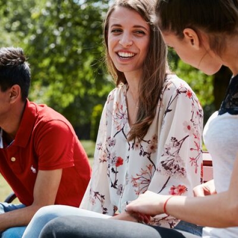 Three students, sitting on a bench in a park, talking and laughing