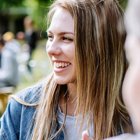 Students chatting at a picnic bench in the park, one wearing a yellow jumper and the other a denim jacket