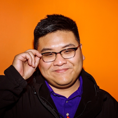 Smiling male student hold glasses in front of orange wall