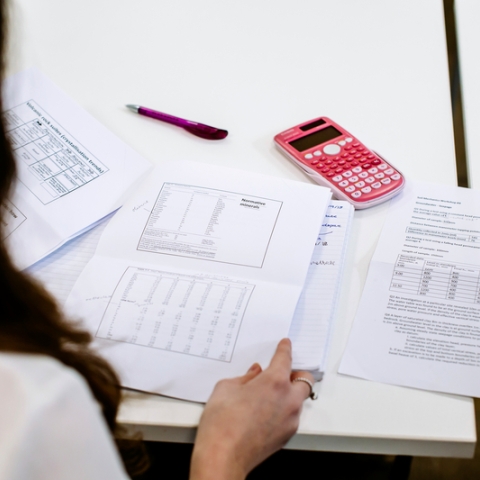 Female student looks over test pages with pink calculator on desk