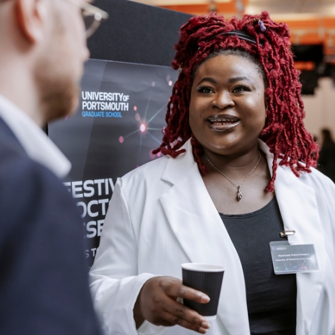 Photo of Rachael Odunmbaku talking with others inside- Festival of Doctoral ResearchFOR GRADUATE SCHOOL USE ONLY