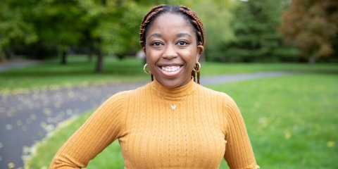 female student smiling in a yellow jumper stood in a park