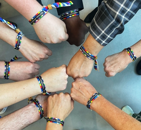 Photo of 10 hands in a circle, all wearing a festival wristband