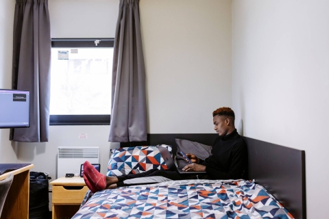 Male student sitting on bed looking at phone