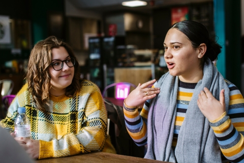 Two students sat talking to each other at a cafe