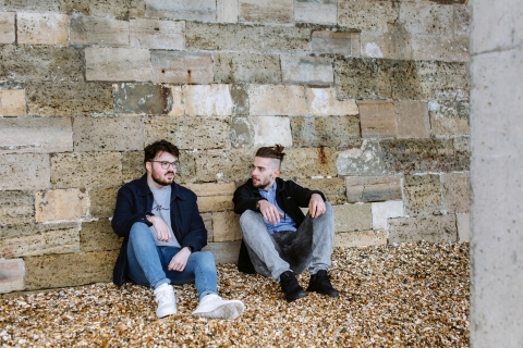 Two male students sat against the walls of Old Portsmouth talking on the beach
