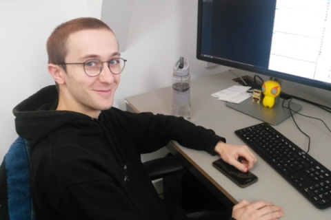 Alex Hayward sitting at computer and smiling at camera