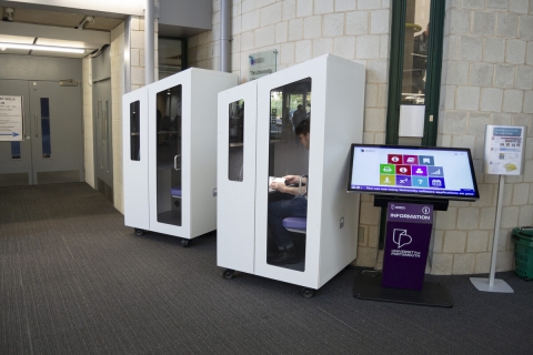 Two individual study pods. White exterior with glass door frame and inside showing purple seat with small desk space.