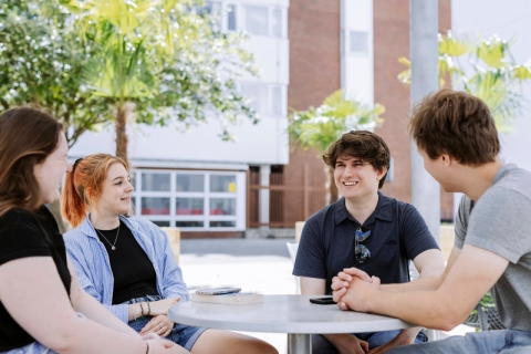 Students talking and relaxing around a table in the Northern Quarter outside of Technology Facilities