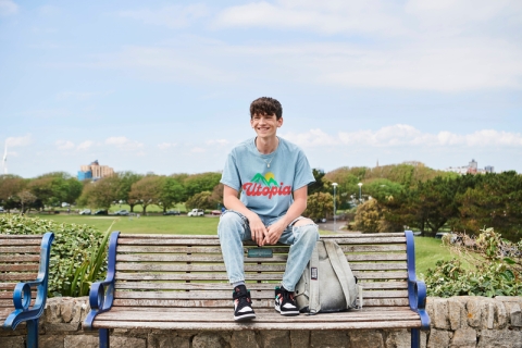 Student sat on bench in blue top and jeans overlooking field