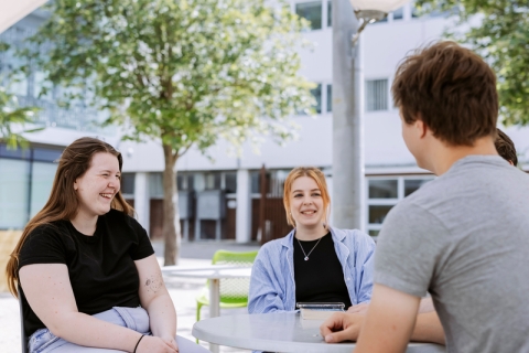 Students talking and relaxing around a table in the Northern Quarter outside of Technology Facilities