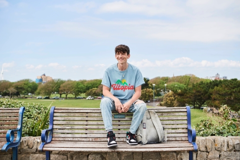 Student sat on bench in blue top and jeans overlooking field