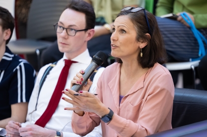 A woman in a pink blouse speaking through a microphone