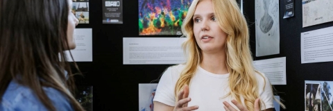 Postgraduate student standing by a poster board explaining the poster 