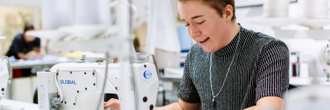 Textiles placement year student working in a fashion company. She is sat at a sewing machine working.