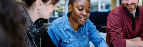 Staff member talking to two students at a table, supporting them with some of their work