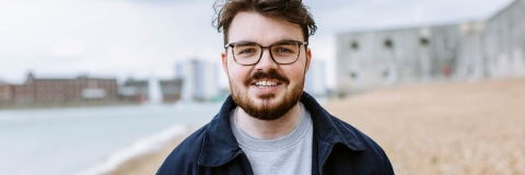 Male student in glasses with beard walking along the stone beach at Old Portsmouth