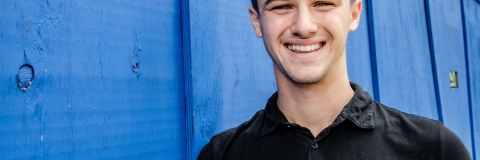 Josh Robinson smiling to camera wearing black t-shirt against blue wall