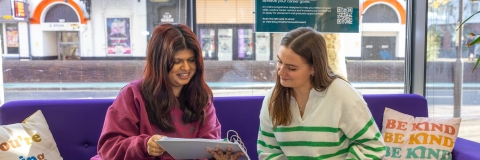 Two students sat on a sofa looking through a folder