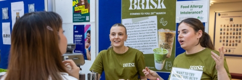 Two girls in green t-shirts talking to a student