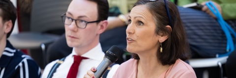 A woman in a pink blouse speaking through a microphone