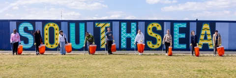 Group of students litter picking on Southsea seafront in front of a sign that reads 'Southsea'