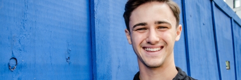 Josh Robinson smiling to camera wearing black t-shirt against blue wall