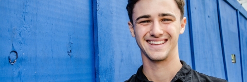 Josh Robinson smiling to camera wearing black t-shirt against blue wall