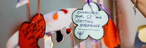 Person hanging up label in the shape of a flower with writing on it about work experience at the volunteering fair