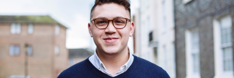 Male in blue jumper and glasses outside smiling at camera