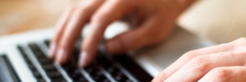 Close-up of hands typing on a laptop keyboard.