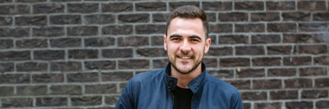 A male student smiling standing in front of a brick wall