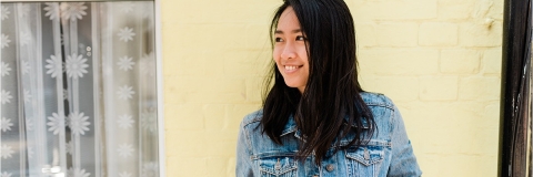 Student looking to her left while leaning against a yellow painted house