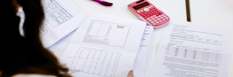 Female student looks over test pages with pink calculator on desk