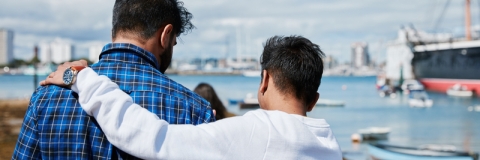 Two people looking out to sea, one with arm around the other