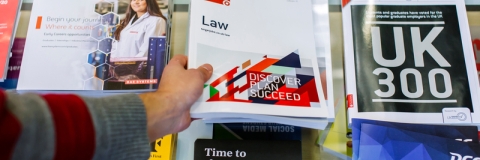 Career guidance books and leaflets on a desk with a person's hand picking one up